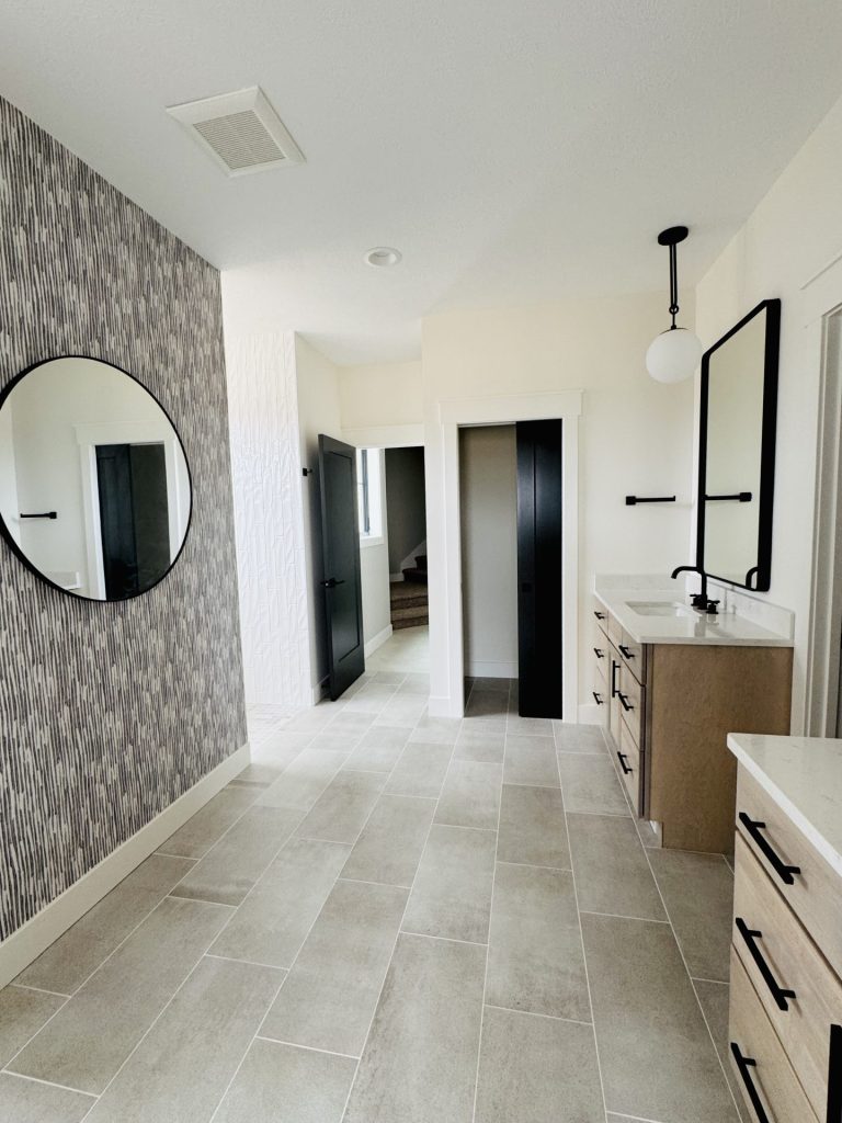 Modern bathroom with a large mirror, textured accent wall, light tile flooring, double sink vanity, and black doors leading to other rooms.