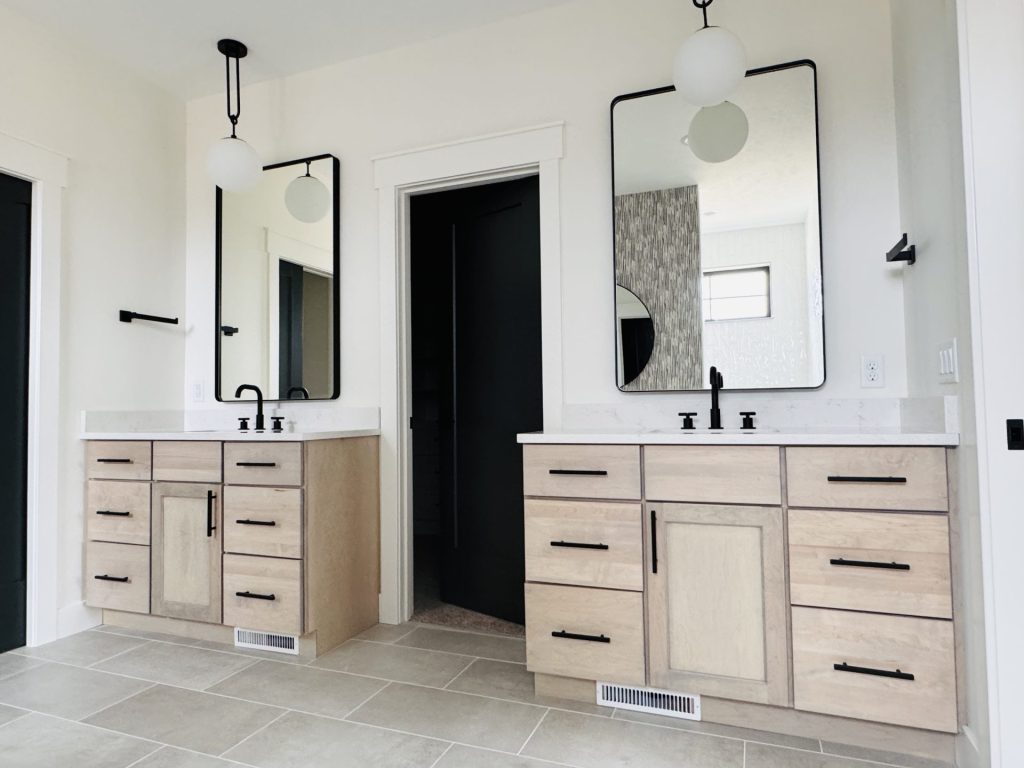 Modern bathroom with double vanities, black fixtures, large rectangular mirrors, light wood cabinets, and light tiled floor.