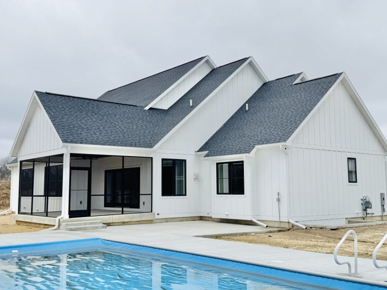 A modern white house with dark roof shingles, large windows, and a screened porch, situated next to a rectangular outdoor swimming pool.