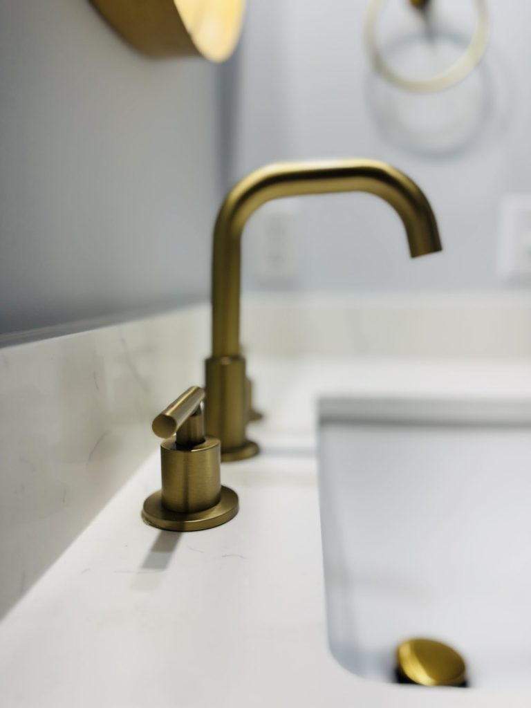 Close-up of a modern bathroom sink with a brushed gold faucet and matching handle on a white countertop.