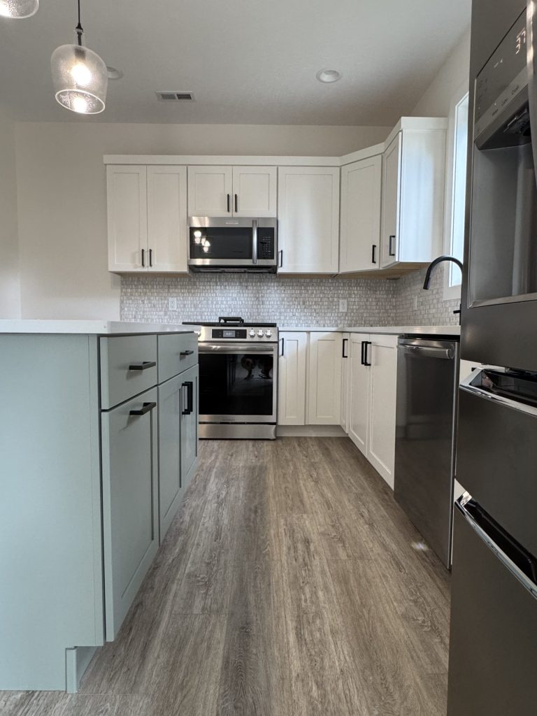 Modern kitchen with white cabinets, stainless steel appliances, light wood flooring, a center island with green cabinetry, and mosaic tile backsplash.